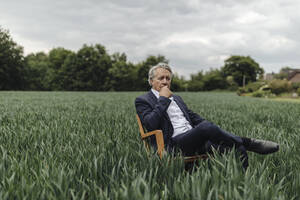 Senior businessman sitting on a chair in a field in the countryside - GUSF04070