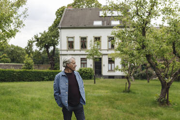 Ein älterer Mann steht in einem ländlichen Garten und schaut sich um - GUSF04092