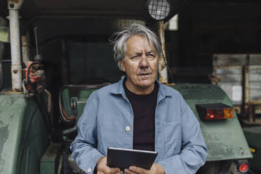 Älterer Mann mit Tablet auf einem Bauernhof mit Traktor in der Scheune - GUSF04100