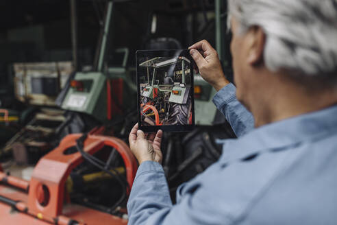 Älterer Mann fotografiert einen Traktor in einer Scheune mit einem Tablet - GUSF04108