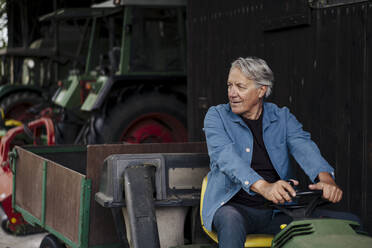Älterer Mann fährt Traktor mit Anhänger auf einem Bauernhof - GUSF04126