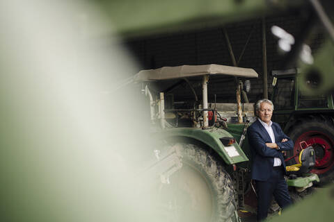 Älterer Geschäftsmann auf einem Bauernhof mit Traktor in einer Scheune, lizenzfreies Stockfoto