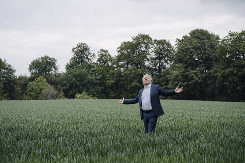 Älterer Geschäftsmann, der mit ausgestreckten Armen auf einem Feld auf dem Lande steht - GUSF04155