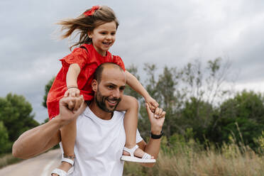 Happy man carrying daughter on shoulders at countryside - EGAF00359