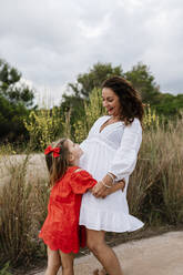 Happy girl embracing mother on country road against cloudy sky - EGAF00361