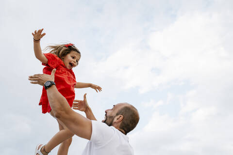 Cheerful father lifting daughter against sky stock photo