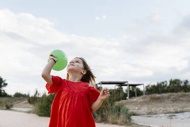 Cute girl playing with balloon at beach against cloudy sky - EGAF00376