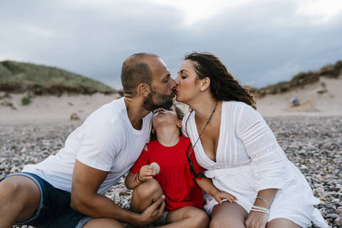 Pärchen küsst sich mit Tochter am Strand, lizenzfreies Stockfoto