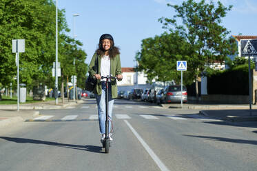 Glückliche junge Frau fährt elektrischen Roller auf der Straße in der Stadt - KIJF03147