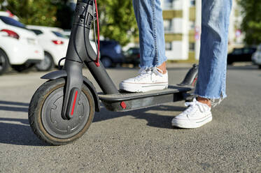 Frau mit elektrischem Tretroller auf der Straße an einem sonnigen Tag - KIJF03158