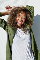 Cheerful woman standing with hands behind head during sunny day - KIJF03162