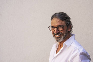 Happy mature man wearing eyeglasses against gray wall - DLTSF00821