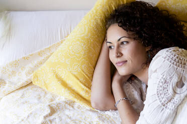 Thoughtful young woman lying on bed in cottage - LVVF00123