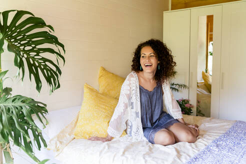 Fröhliche junge Frau sitzt auf dem Bett in einer Blockhütte - LVVF00124