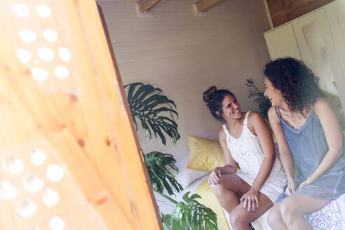 Glückliche junge Freundinnen unterhalten sich in einem Haus, gesehen durch ein Fenster - LVVF00132