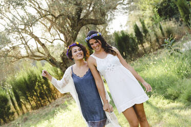 Happy female friends wearing wreaths while walking at yard - LVVF00136