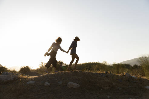 Freundinnen halten sich an den Händen, während sie auf einem Hügel auf dem Land spazieren gehen - LVVF00151