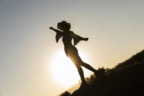 Junge Frau steht mit ausgestreckten Armen auf einem Hügel vor einem klaren Himmel - LVVF00154