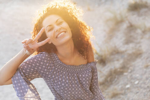Fröhliche junge Frau mit Friedenszeichen an einem sonnigen Tag - LVVF00160