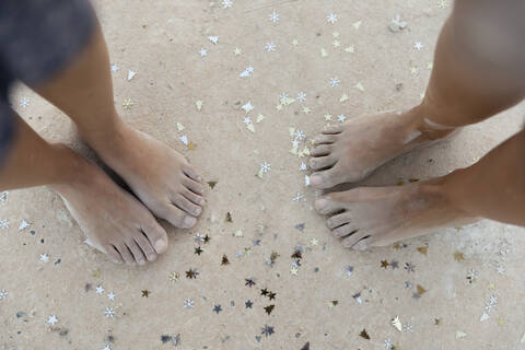Female friends standing with Christmas confetti on sand stock photo