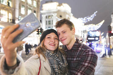 Frau nimmt Selfie mit Freund gegen Weihnachtsbeleuchtung in der Stadt bei Nacht - WPEF03119