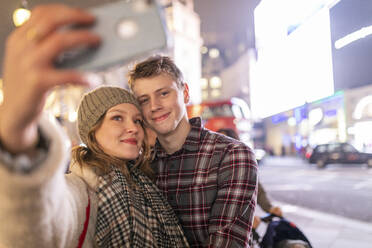 Junge Frau nimmt Selfie mit Freund, während in beleuchteten Stadt in der Nacht stehen - WPEF03126