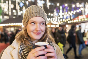 Nahaufnahme einer schönen Frau mit heißer Schokolade auf dem Weihnachtsmarkt bei Nacht - WPEF03135