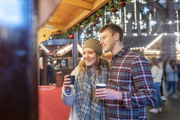 Couple enjoying hot chocolates in Christmas market at night - WPEF03136