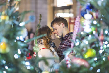 Young couple romancing while standing by illuminated Christmas tree at night - WPEF03142