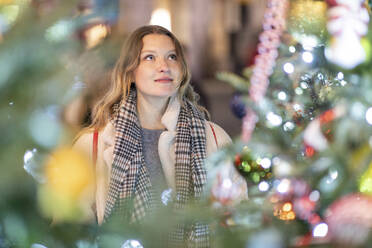 Junge Frau betrachtet beleuchteten Weihnachtsbaum und Lichter in der Stadt - WPEF03144