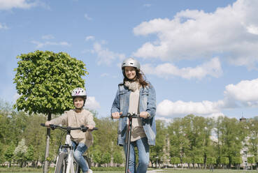 Mädchen auf dem Fahrrad, während die Mutter auf dem Motorrad gegen den Himmel im Stadtpark fährt - AHSF02779