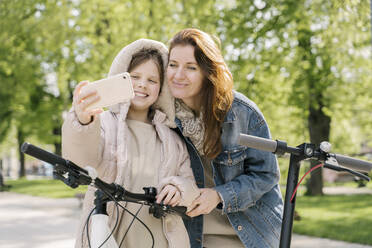 Mädchen, das ein Selfie mit seiner Mutter macht, während es im Stadtpark an einem Baum steht - AHSF02789