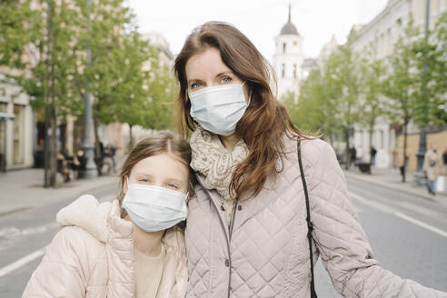 Mother and daughter wearing masks standing on street in city - AHSF02796