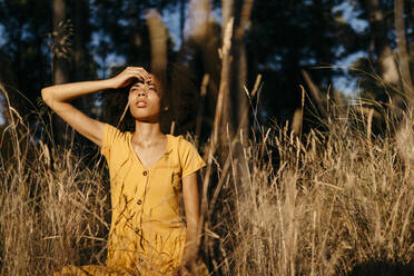 Nachdenkliche junge Frau, die wegschaut, während sie inmitten von Pflanzen im Wald sitzt - TCEF00867