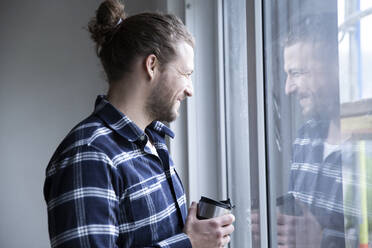 Construction worker holding container looking through window at home - MJFKF00385