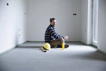 Construction worker sitting on floor in empty house at construction site - MJFKF00388