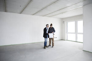Architekt und Bauarbeiter besprechen einen Bauplan, während sie in einem leeren Haus stehen - MJFKF00417