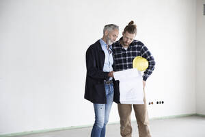 Architekt und Bauarbeiter besprechen einen Bauplan, während sie in einem leeren Haus stehen - MJFKF00418