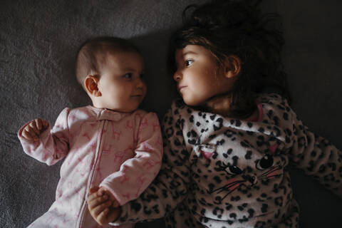 Niedliche Schwestern, die sich gegenseitig anschauen, während sie auf dem Bett liegen, lizenzfreies Stockfoto