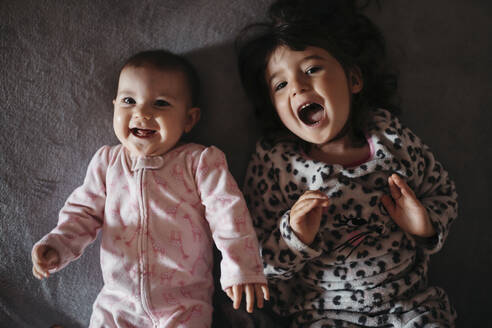 Fröhliche süße Schwestern schreien, während sie zu Hause auf dem Bett liegen - GEMF03917