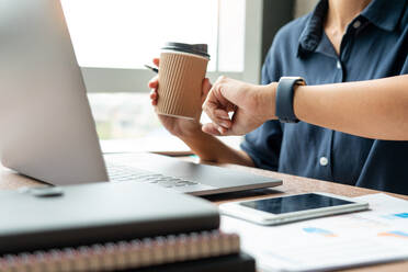 Midsection Of Businessman Holding Disposable Cup While Checking Time On Table - EYF09169