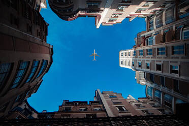 Low Angle View Of Airplane Flying Over Buildings Against Blue Sky - EYF09376