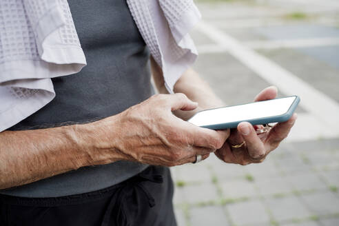 Nahaufnahme eines älteren Mannes, der ein Mobiltelefon benutzt, während er im Freien steht - MEUF01158