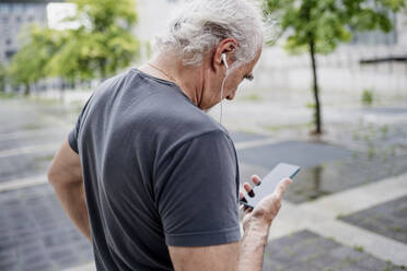 Close-up of senior man using smart phone listening music while standing outdoors - MEUF01165