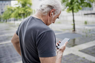 Nahaufnahme eines älteren Mannes, der ein Smartphone benutzt und Musik hört, während er im Freien steht - MEUF01165