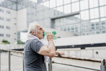 Älterer Mann trinkt Wasser, während er an einem Geländer in der Stadt steht - MEUF01169