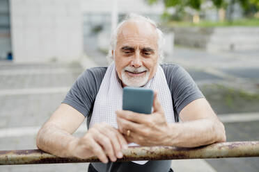 Nahaufnahme eines älteren Mannes, der ein Smartphone benutzt, während er an einem Geländer steht - MEUF01171