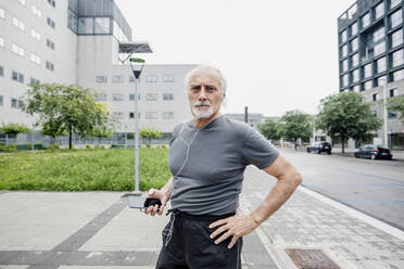 Selbstbewusster älterer Mann hört Musik, während er auf einem Fußweg in der Stadt steht - MEUF01178