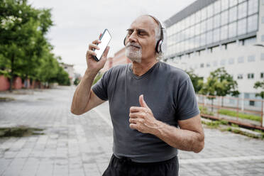 Senior woman with eyes closed listening music while standing on footpath in city - MEUF01191