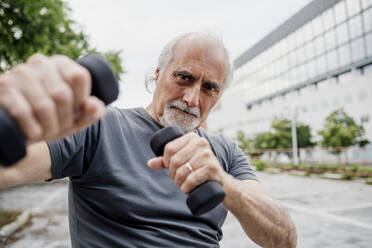 Close-up of confident senior man holding dumbbells while standing in city - MEUF01194